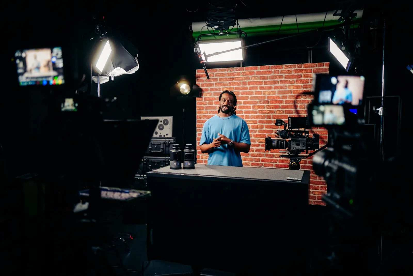 Moderator vor Ziegelwand beim Dreh der Videoreihe, im Vordergrund Kamera und Monitore