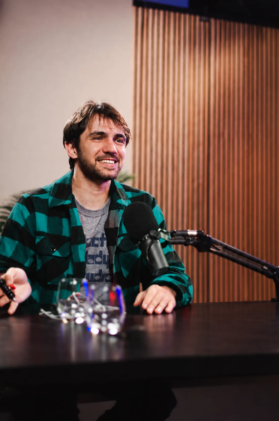 Anto Petricevic lacht am Podcast-Tisch vor einer Holzlamellenwand