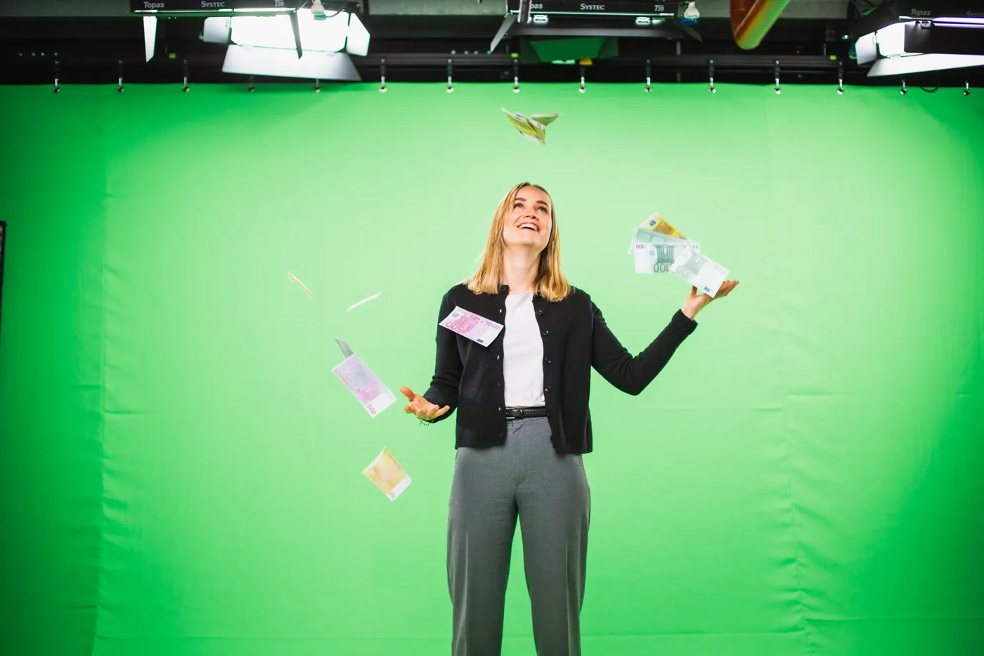 Protagonistin wirft vor dem Greenscreen lachend Geldscheine in die Luft